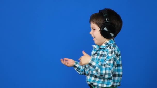 Yaşında Kulaklıklı Bir Çocuk Mavi Arka Planda Sevinçle Üzüntüyle Ellerini — Stok video