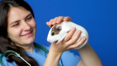 Veteriner elinde küçük bir kobay tutuyor, okşuyor ve gülümsüyor.