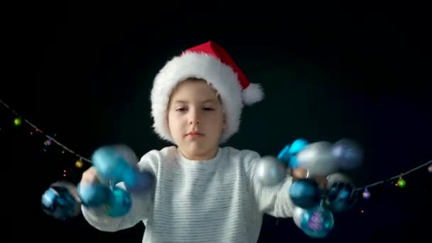 一个戴着桑塔帽子的快乐的5岁男孩 带着蓝色的圣诞球玩得很开心 — 图库视频影像