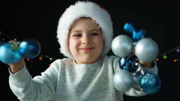 一个戴着桑塔帽子的快乐的5岁男孩 带着蓝色的圣诞球玩得很开心 — 图库视频影像
