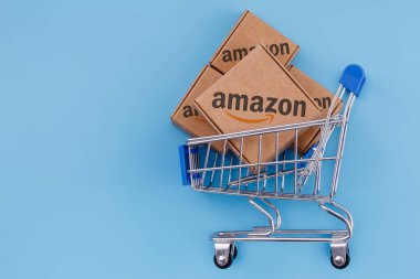 Kazan, Rusya - Ekim 02, 2021: Amazon dünyanın en büyük e-ticaret platformu pazarlarından biri olan bir Amerikan şirketidir. Alışveriş arabasında Amazon logosu olan paketin değiştirilmiş fotoğrafı mavi arka planda.