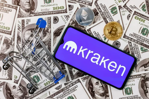 Kazan, Rusya - 12 Ekim 2021 Kraken kripto para değişimi. Üzerinde Kraken logosu olan akıllı bir telefon, bir alışveriş arabası ve dolar banknotlarında kripto paralar.. 