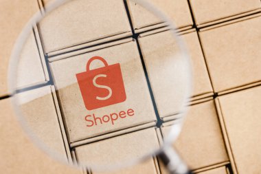 Kazan, Rusya - 14 Ekim 2021 Shopee bir e-ticaret teknoloji şirketidir. Paketlerle çevrili bir büyüteç altındaki kutunun üzerindeki Shopee logosunun değiştirilmiş fotoğrafı..