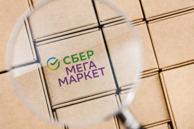 Kazan, Rusya - 18 Ekim 2021: SberMegaMarket, Sberbank 'a ait bir Rus pazarı. SberMegaMarket logosunun değiştirilmiş fotoğrafı bir büyüteç altında paketlerle çevrili bir kutunun üzerinde.