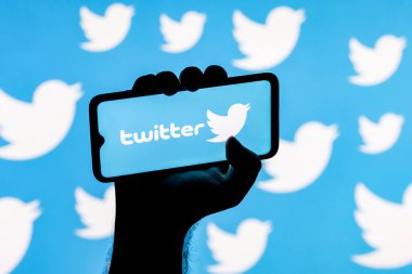 Kazan, Rusya - 23 Ekim 2021: Twitter sosyal ağ logosuna sahip akıllı telefon Twitter logolarının arka planında sıkışık bir elle