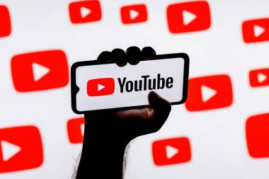 Kazan, Rusya - 24 Ekim 2021: Youtube sosyal medya platformunun logosuna sahip akıllı telefon Youtube logolarının arka planında sıkışık bir elle ekranda