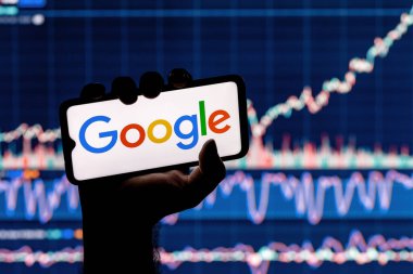Kazan, Rusya - 26 Ekim 2021: Google teknoloji şirketi logosu olan bir akıllı telefon. Arkaplanda Google borsa grafiği.