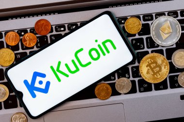 Kazan, Rusya - 26 Ekim 2021: KuCoin şifreli para değişimi. Üzerinde KuCoin logosu olan bir akıllı telefon metal paralar, bitcoin, bir dizüstü bilgisayar klavyesinde ethereum..