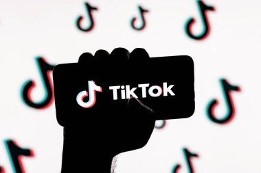 Kazan, Rusya - 31 Ekim 2021: Ekranda TikTok sosyal ağ logosu olan akıllı telefon TikTok logolarının arka planında sıkışık bir elle