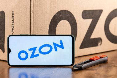 Kazan, Rusya - 28 Aralık 2020: Ozon logosu ekranda yakın plan akıllı telefon. Özon, Rusya 'daki ilk e-ticaret şirketlerinden biri. Paket ve maket kesicinin arka planında akıllı telefon var.