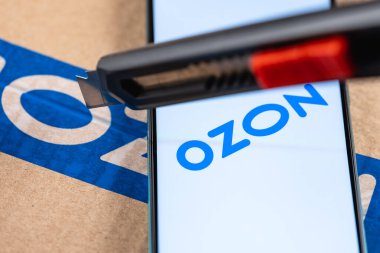 Kazan, Rusya - 28 Aralık 2020: Ozon logosu ekranda yakın plan akıllı telefon. Paketin arka planında akıllı telefon var. Paket maket bıçağıyla açılıyor.. 