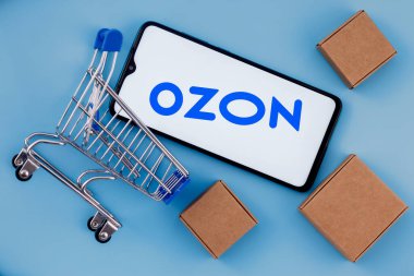 Kazan, Rusya - 10 Kasım 2021: Ozon Rus e-ticaret şirketidir. Ekranda Ozon logosu olan akıllı telefon, alışveriş arabası ve paketler..