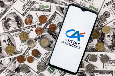 Kazan, Rusya - 16 Aralık 2021: Dolar banknotlarının arka planında çeşitli metal paralarla çevrili Credit Agricole banka logosu olan akıllı telefon