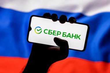 Kazan, Rusya - 27 Ocak 2021: Sberbank logosu ile Rusya bayrağının arka planında sıkışmış akıllı telefon