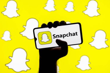 Kazan, Rusya - 30 Ocak 2022: Snapchat anlık mesajlaşma servisi logosu ile Snapchat logolarının arka planında sıkışmış bir elle ekranda akıllı telefon