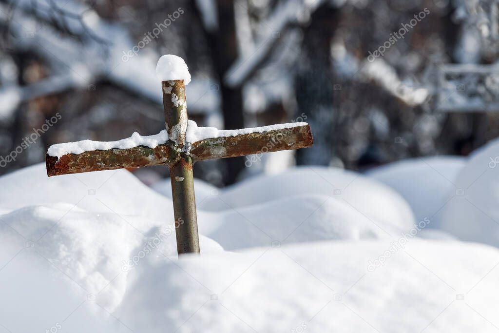 Dilapidated homemade metal crucifix in snowdrift in cemetery