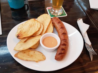 Yanında patates ve sosis olan bir tabak resmi.