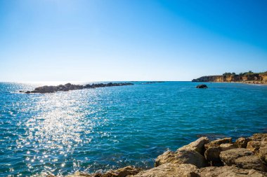 Anzio sahilinin Panorama 'sı Tyrhenian Denizi' nde, plajı ve arkeolojik alanı uzakta. Yazın kayalıklarda mavi gökyüzü ve su üzerindeki ışınlar. Lazio sahilleri, Lazio, İtalya.