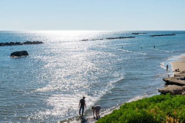 Günbatımından önce banyocularla Anzio plajı. Yazın kayalıklarda mavi gökyüzü ve su üzerindeki ışınlar. Lazio kıyısında, Roma, Lazio, İtalya yakınlarında..