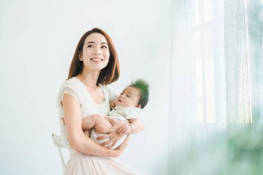 Asyalı anne aydınlık odada bebeği tutuyor.