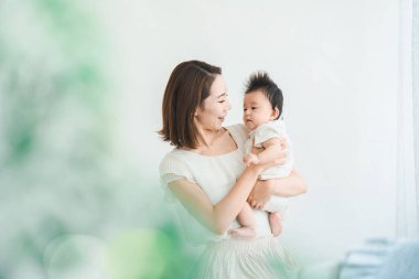 Asyalı anne aydınlık odada bebeği tutuyor.