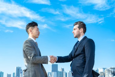 İş adamları güzel bir günde mavi gökyüzü ve binaların zemininde el sıkışıyor.