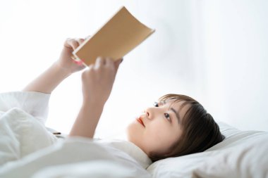 Genç bir kadın yatakta kitap okuyor.
