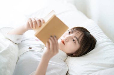 Genç bir kadın yatakta kitap okuyor.