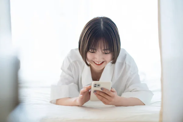 ベッドの上でスマートフォンを操作する若い女性 — ストック写真