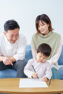 Kalemle çizim yapan bir çocuk ve ailesi ona bakıyor.