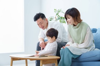 Kalemle çizim yapan bir çocuk ve ailesi ona bakıyor.