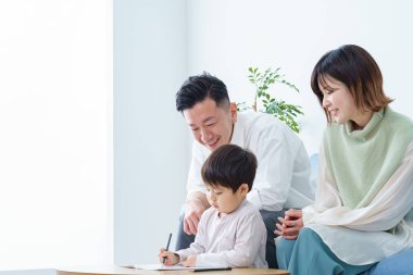 Kalemle çizim yapan bir çocuk ve ailesi ona bakıyor.