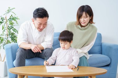 Kalemle çizim yapan bir çocuk ve ailesi ona bakıyor.