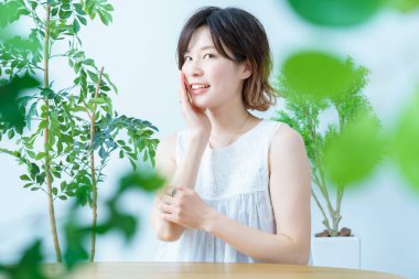 Etrafı yapraklarla çevrili olan ve cildinin durumunu kontrol eden bir kadın.