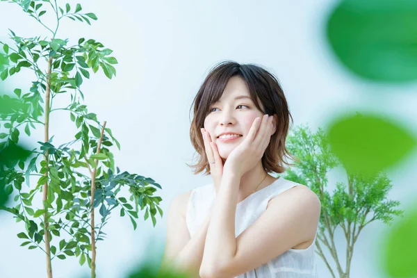 Etrafı yapraklarla çevrili olan ve cildinin durumunu kontrol eden bir kadın.