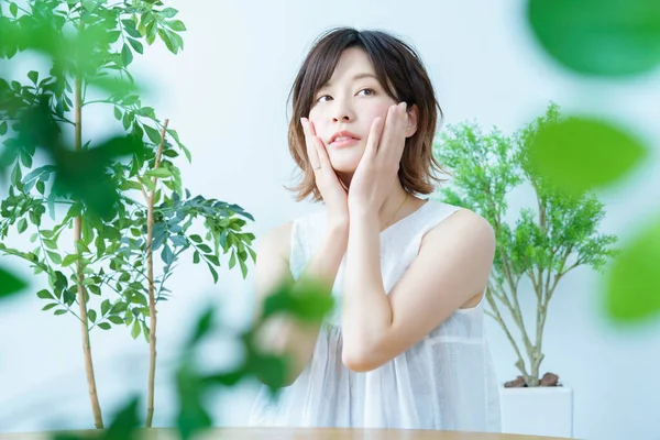 Etrafı yapraklarla çevrili olan ve cildinin durumunu kontrol eden bir kadın.