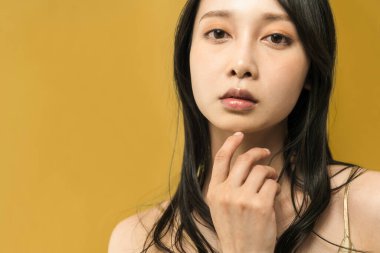 Altın bir arka planın önünde duran siyah saçlı kadın.