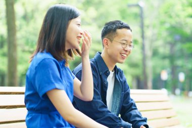 Yeşil bir parkta bankta sohbet eden genç bir çift.