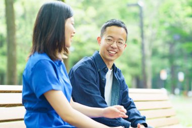 Yeşil bir parkta bankta sohbet eden genç bir çift.