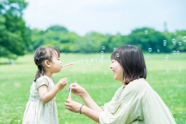Anne ve kızı parkta sabun köpüğüyle oynuyorlar.