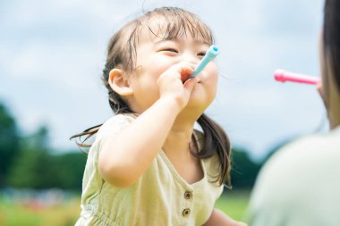 Anne ve kızı parkta sabun köpüğüyle oynuyorlar.