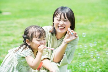 Anne ve kızı parkta sabun köpüğüyle oynuyorlar.