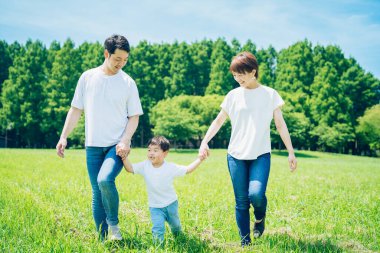 Ebeveynler ve çocukları el ele tutuşup güneşli yeşil bir alanda yürüyorlar.