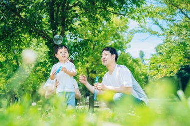 Ebeveynler ve çocukları parkta sabun köpüğüyle oynuyorlar.