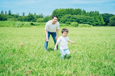 A boy running in the meadow and a father watching over on fine day