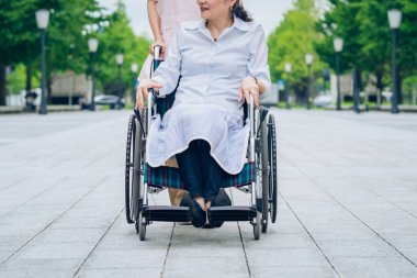 Tekerlekli sandalyede bir kadın ve dışarıda ilgilenecek önlüklü bir kadın.