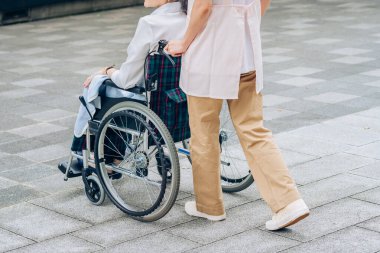 Tekerlekli sandalyede bir kadın ve dışarıda ilgilenecek önlüklü bir kadın.