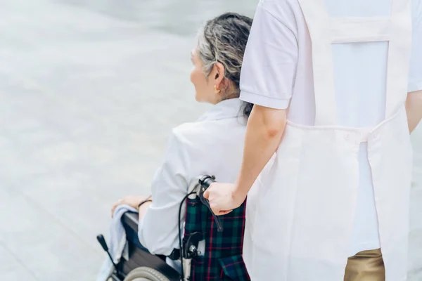 A woman in a wheelchair and a woman in an apron to care for outdoors