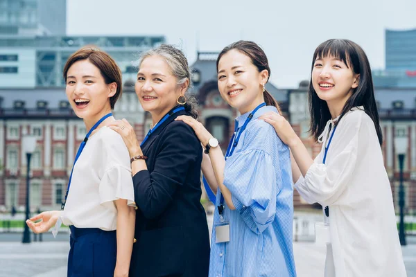 four business women lined up with smiles outdoors