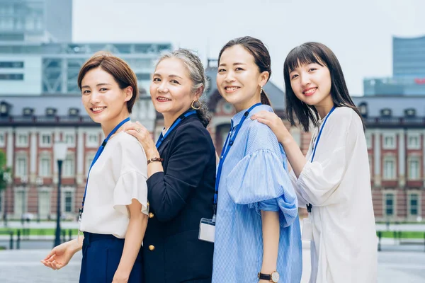 four business women lined up with smiles outdoors